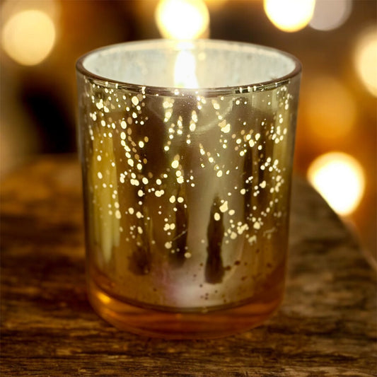 Glass candle holder with glowing interior on a wooden surface with blurred lights in the background