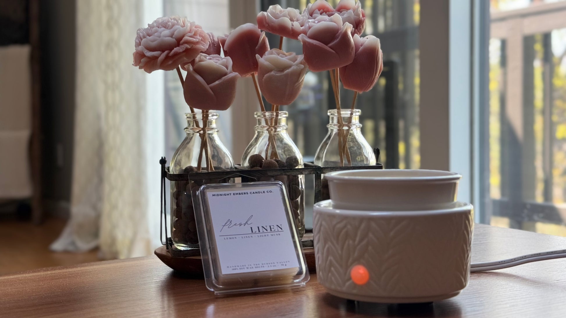 A wax melt in a white holder with a container of fresh linen scent beads in the background on a wooden surface.