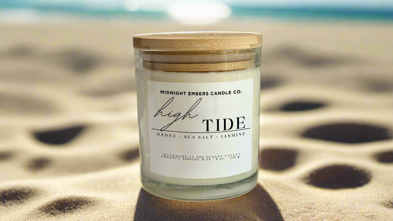 Candle with a wooden lid on a white surface with greenery and rocks in the background