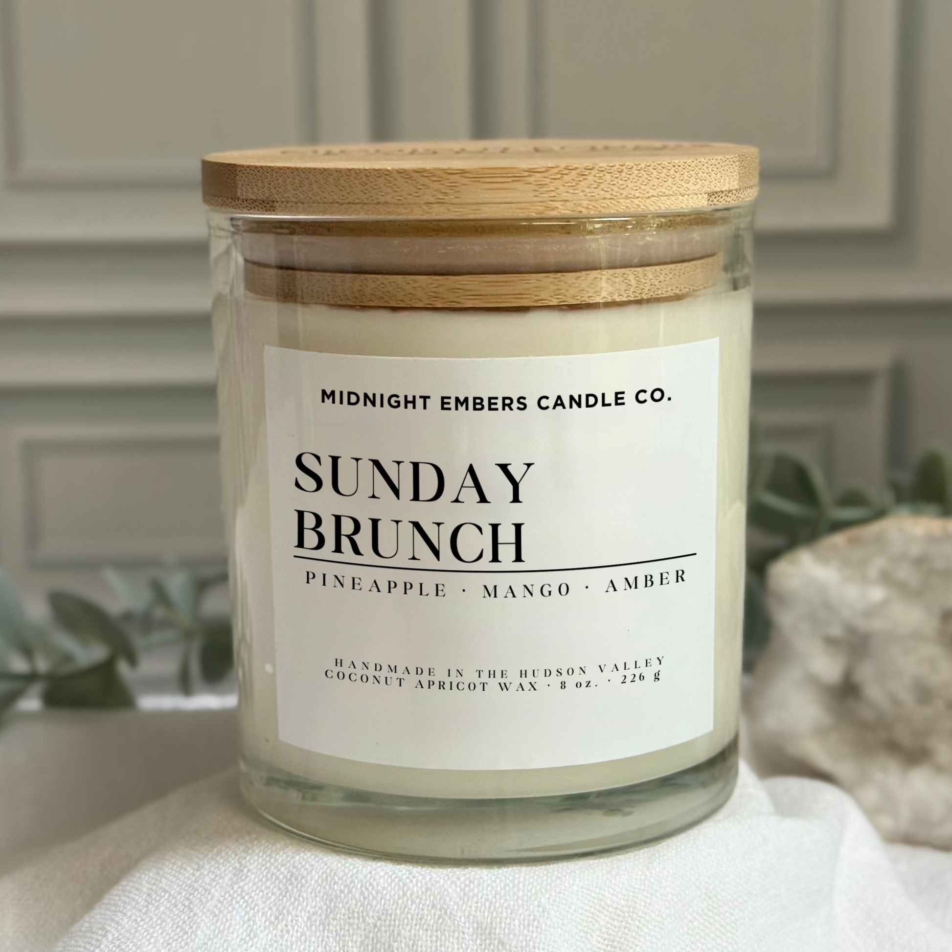 Candle labeled 'Sunday Brunch' from Midnight Embers Candle Co. on a white surface with decorative elements.