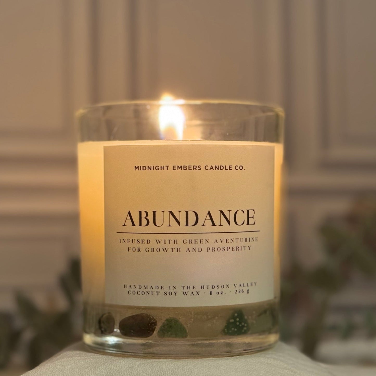 Candle labeled 'Abundance' from Midnight Embers Candle Co. on a surface with a blurred background.