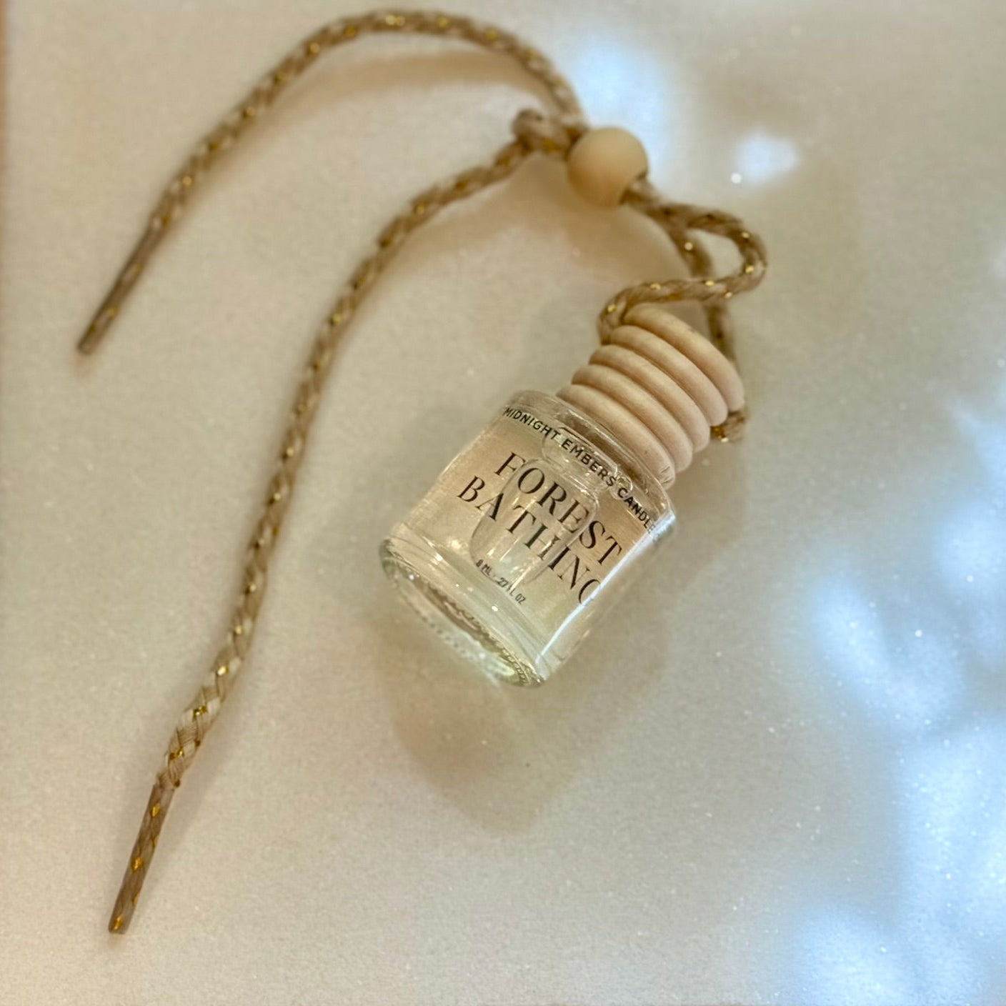 Car diffuser bottle pendant on a chain with a wooden bead, on a light background.