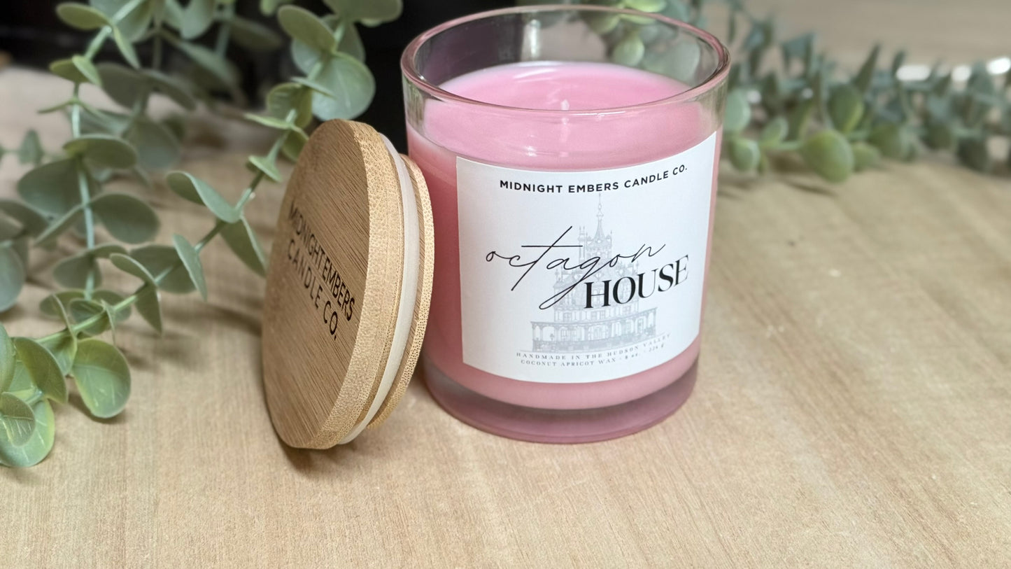 Pink candle with a wooden lid on a wooden surface with greenery in the background