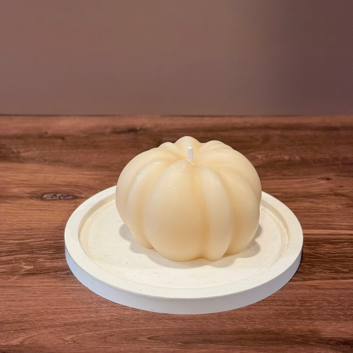 White pumpkin-shaped candle on a wooden surface