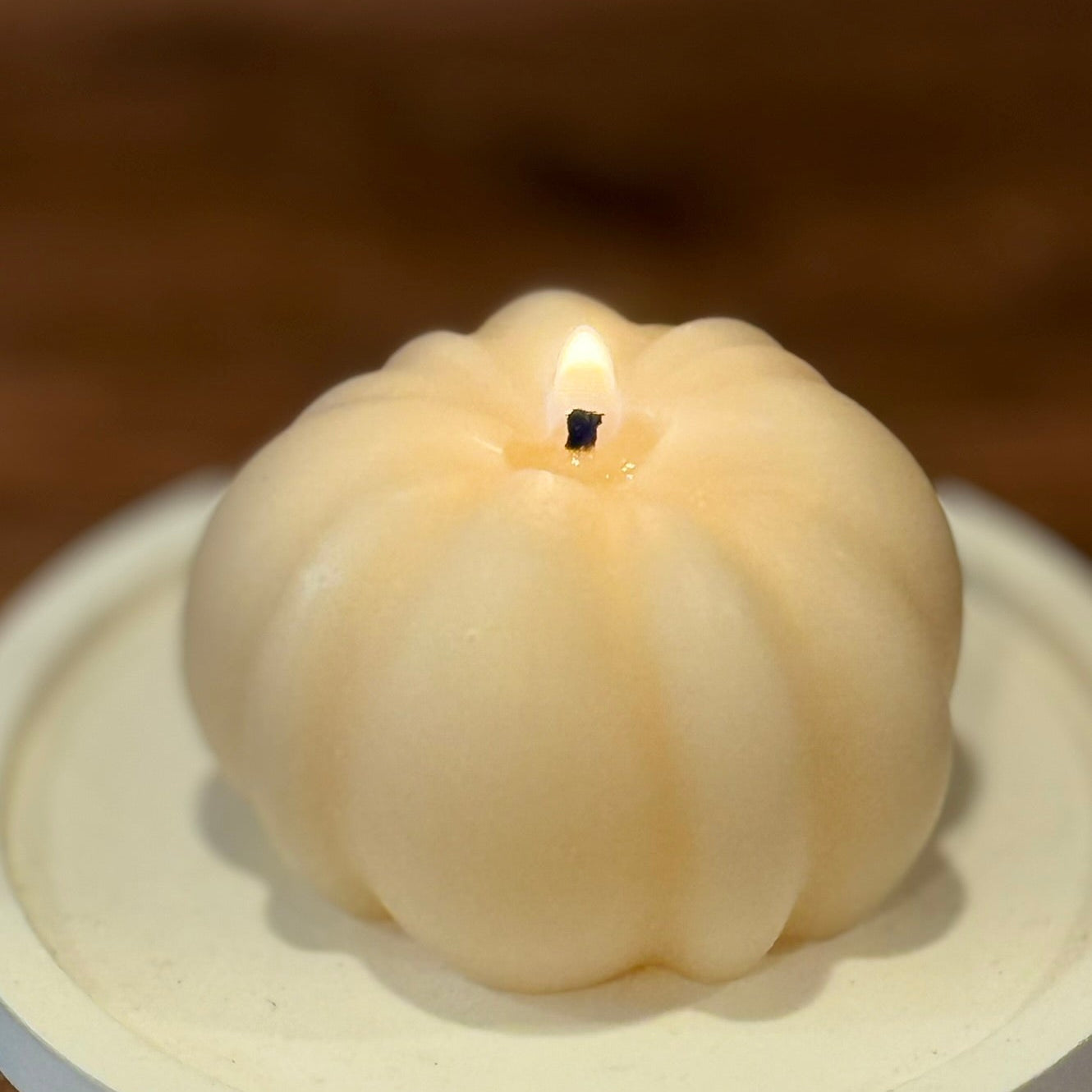 White pumpkin-shaped candle on a wooden surface with a blurred background