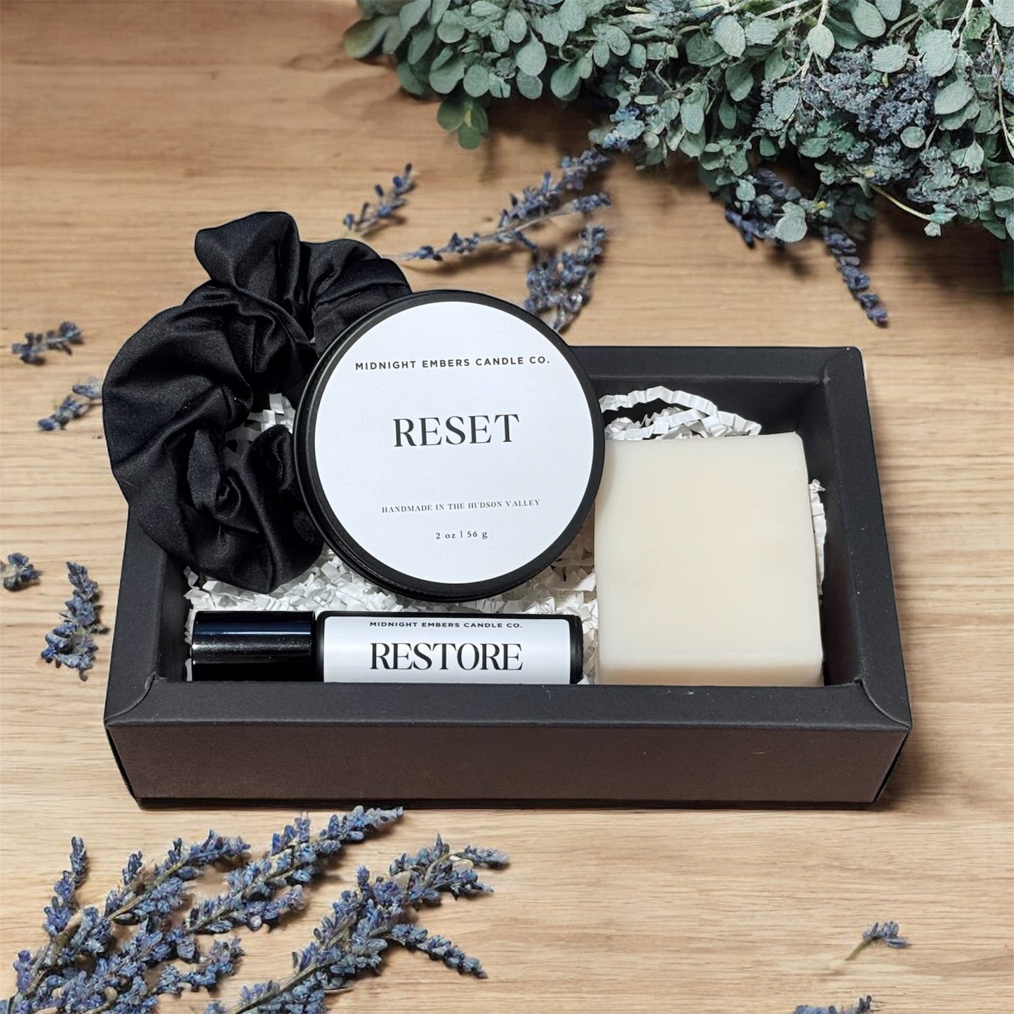 Gift set with candle, soap, and rollerball on a wooden surface with lavender flowers.