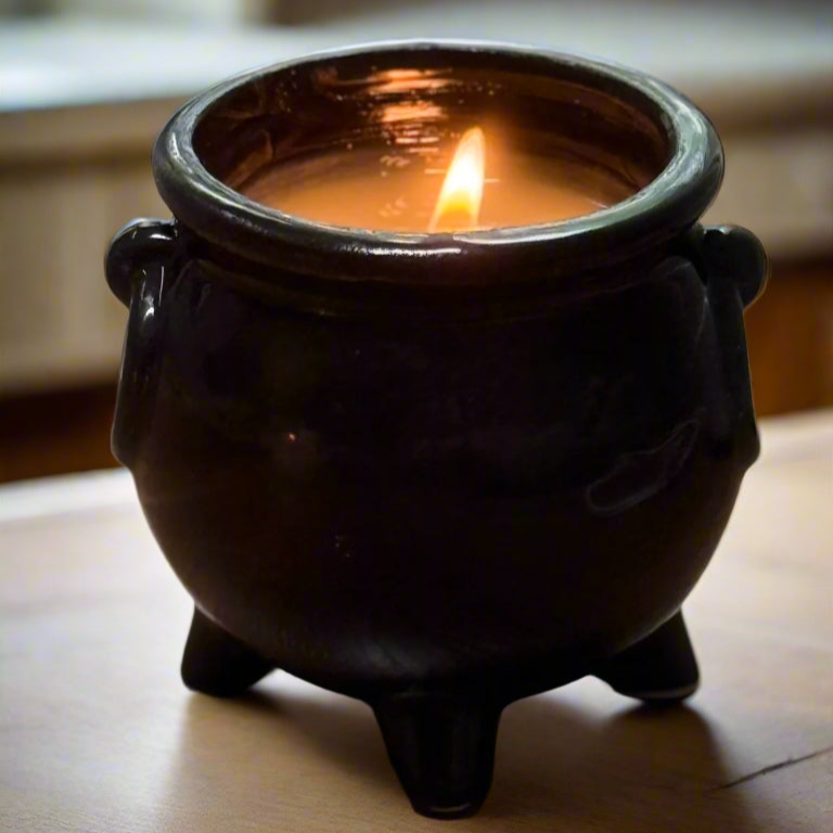 Candle in a black ceramic cauldron on a wooden surface