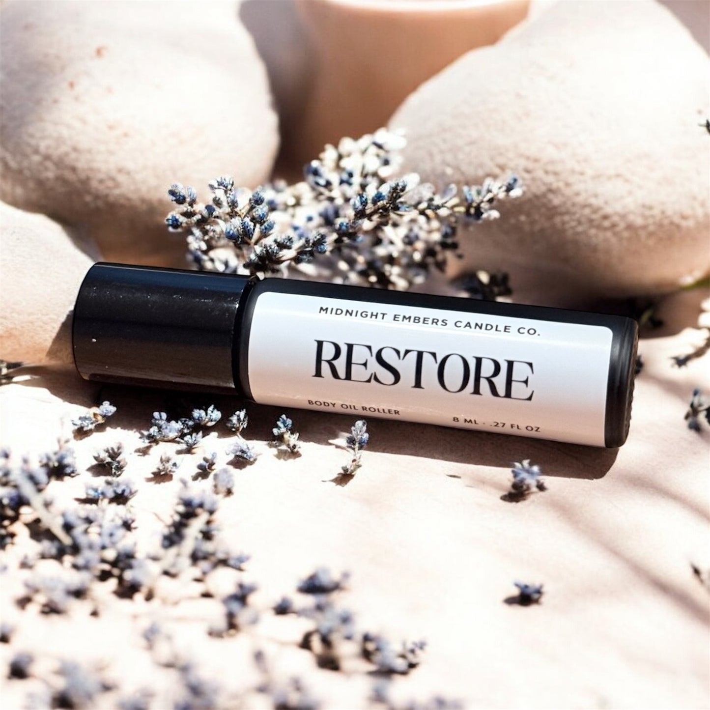 Roller bottle labeled 'Restore' from Midnight Embers Candle Co. on a textured surface with lavender flowers.