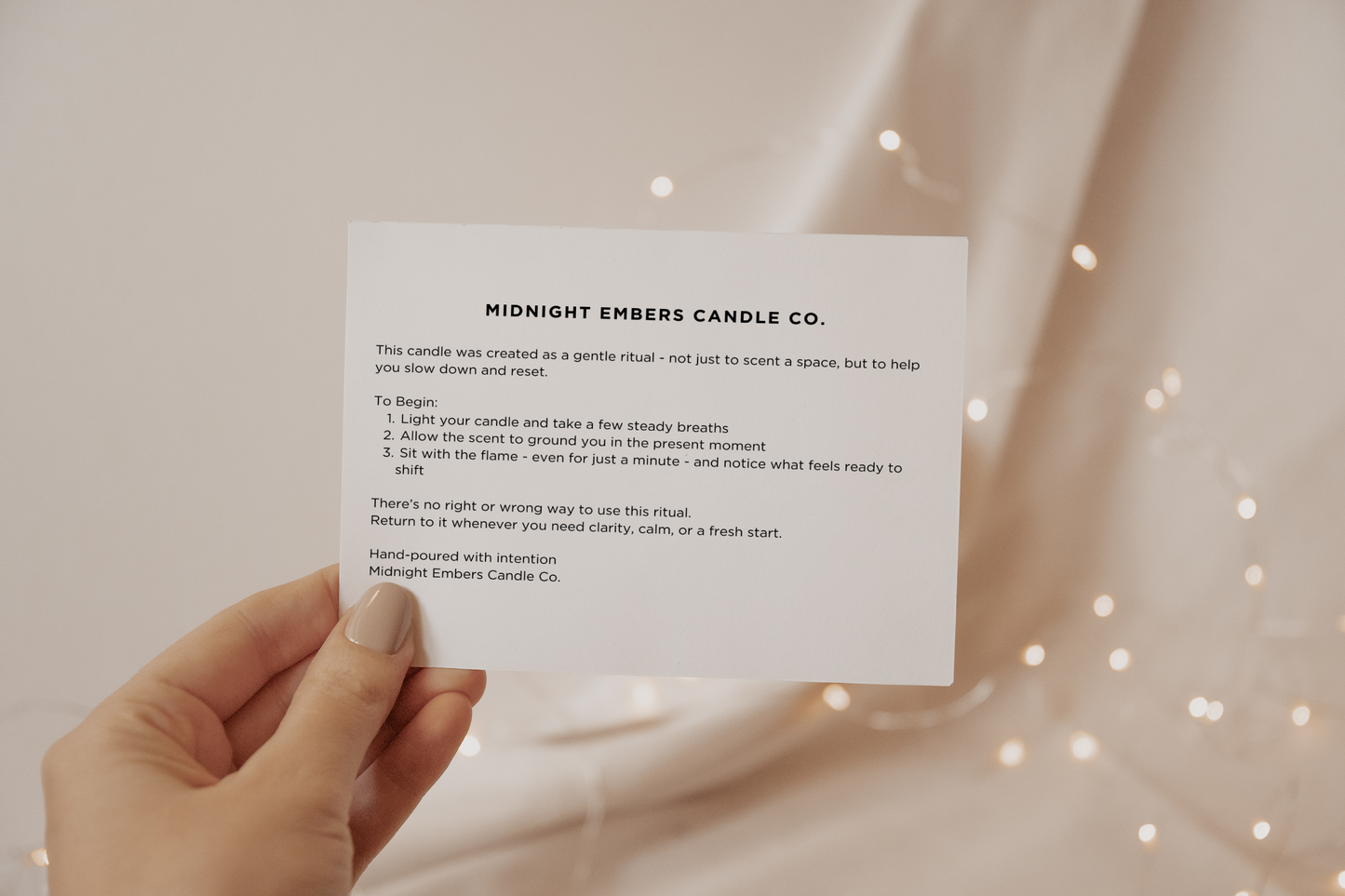 Hand holding a card from Midnight Embers Candle Co. with text on a soft background