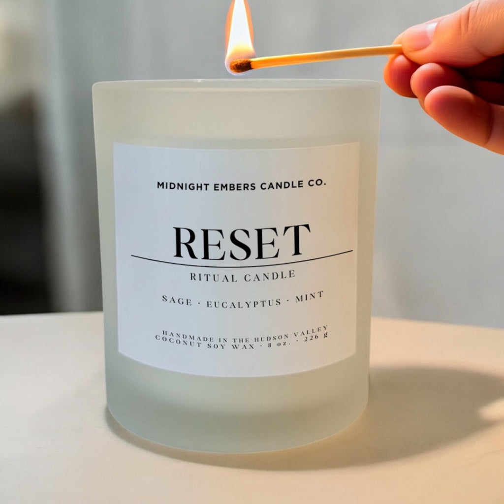 Candle labeled 'Reset' being lit with a match, featuring Midnight Embers Candle Co. branding.