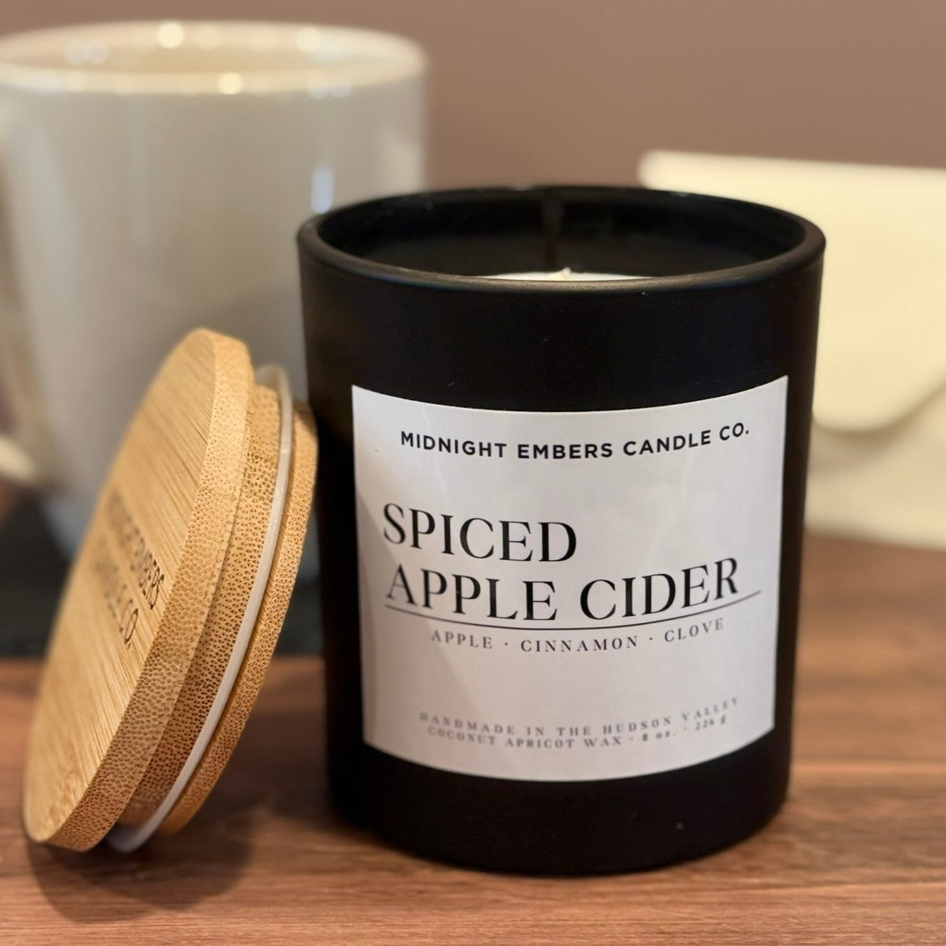Spiced apple cider candle with a mug and coaster on a wooden surface Cozy Fall Aesthetic