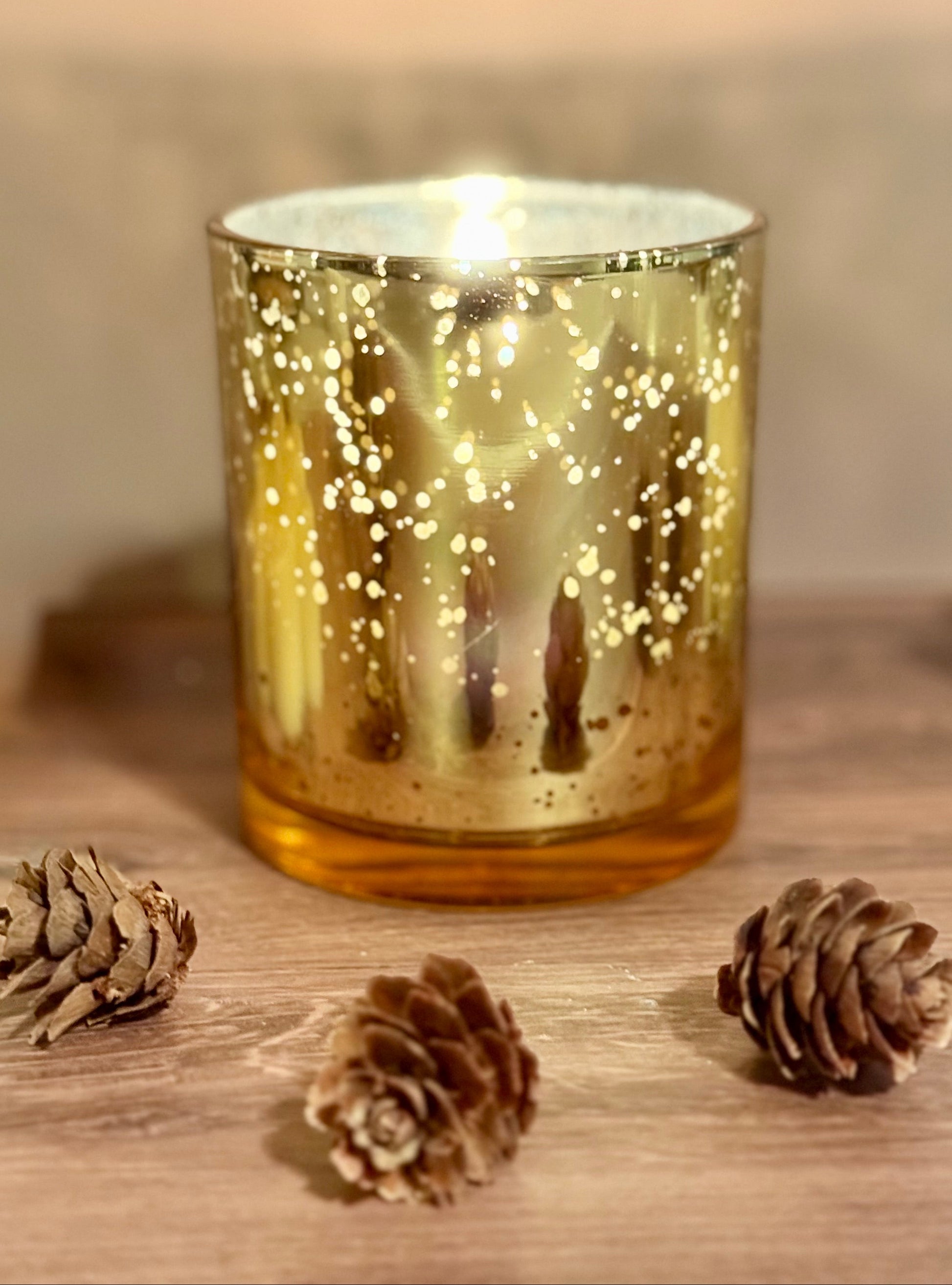 Candle in a gold glass holder with pinecones on a wooden surface