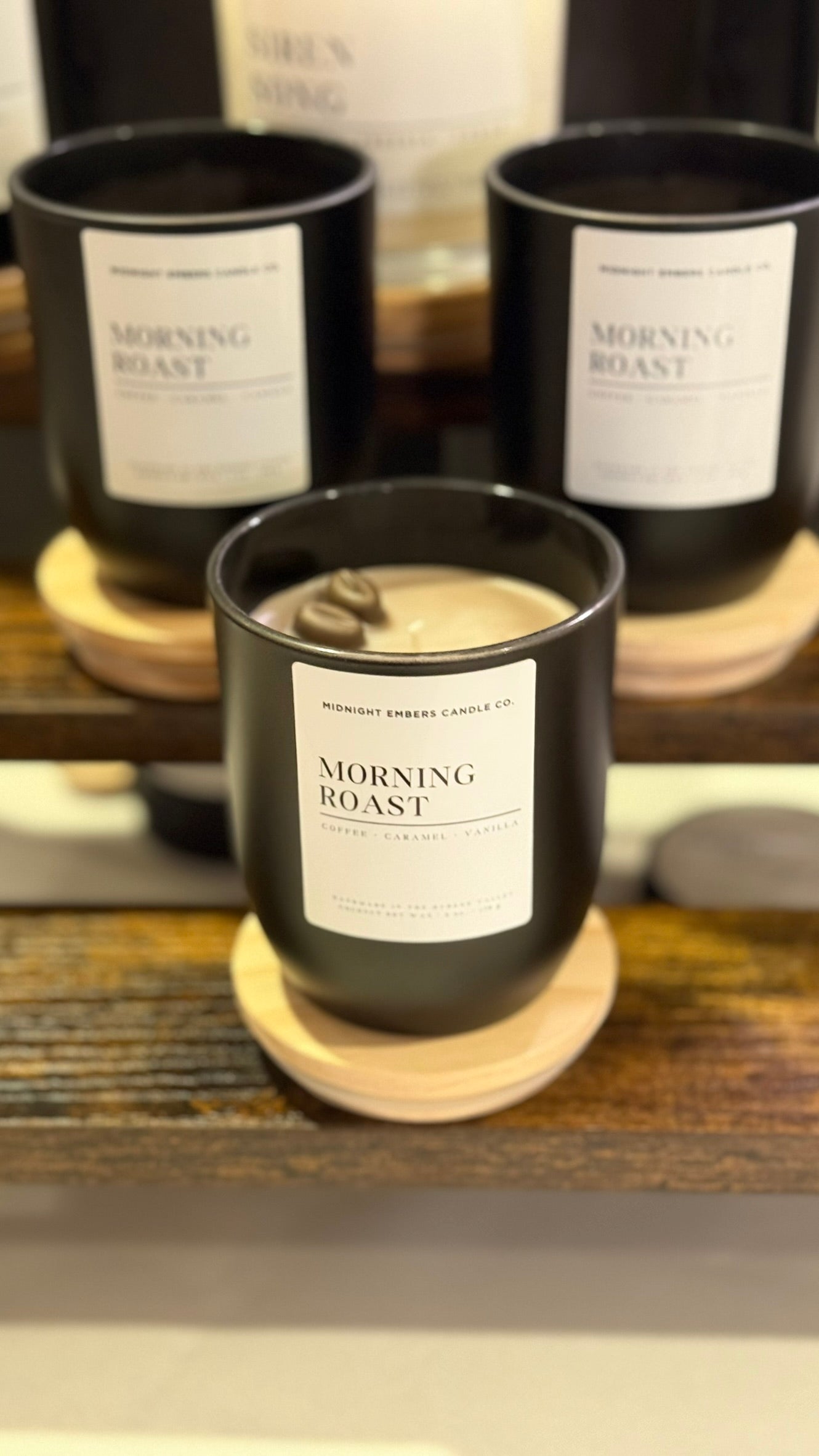 Candle labeled 'Morning Roast' on a wooden coaster with similar candles in the background.