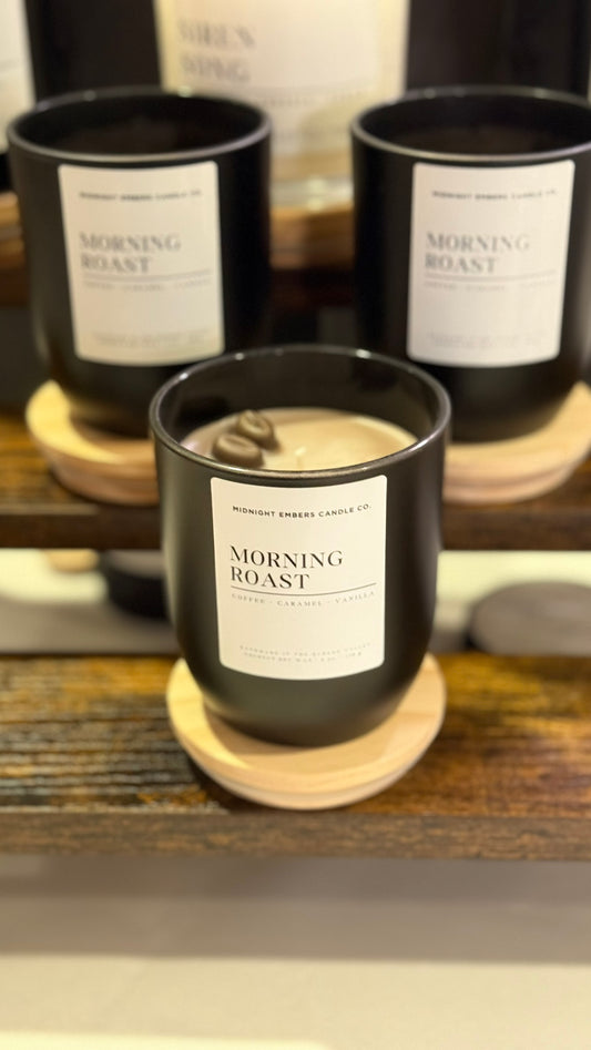 Candle labeled 'Morning Roast' on a wooden coaster with similar candles in the background.