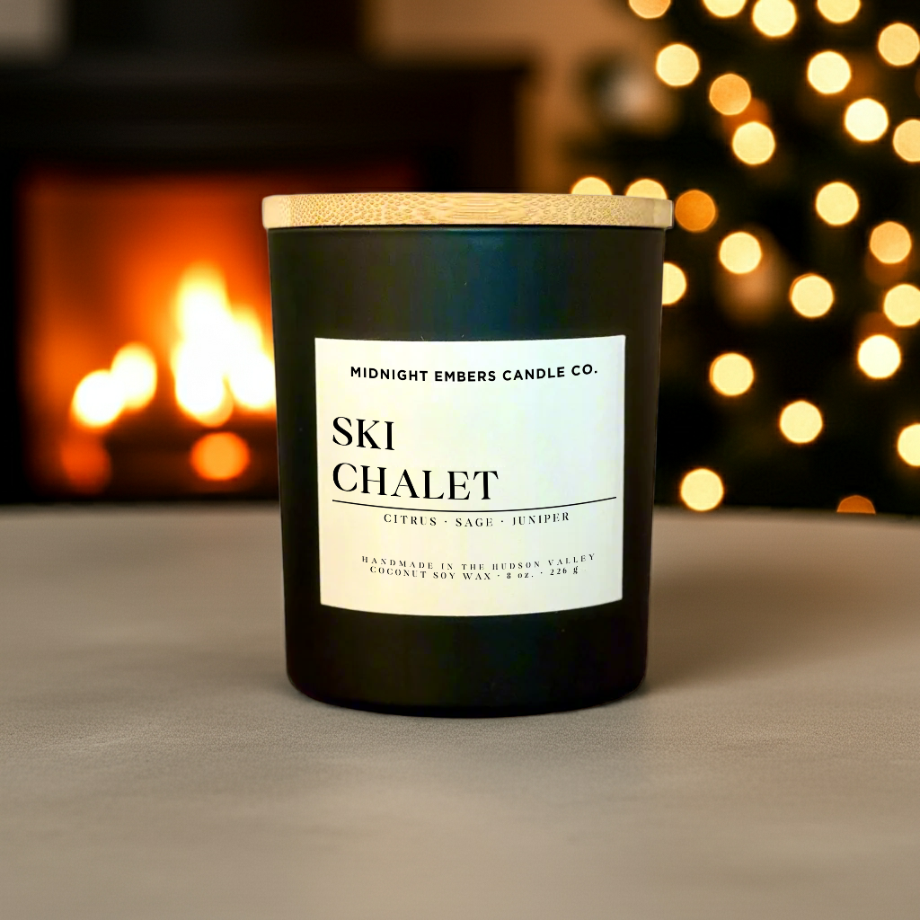 Candle labeled 'Ski Chalet' by Midnight Embers Candle Co. with a fireplace and lights in the background.