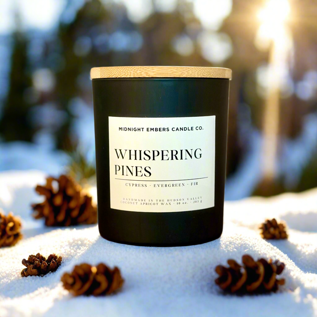 Candle labeled 'Whispering Pines' from Midnight Embers Candle Co. on a snowy background with pinecones.
