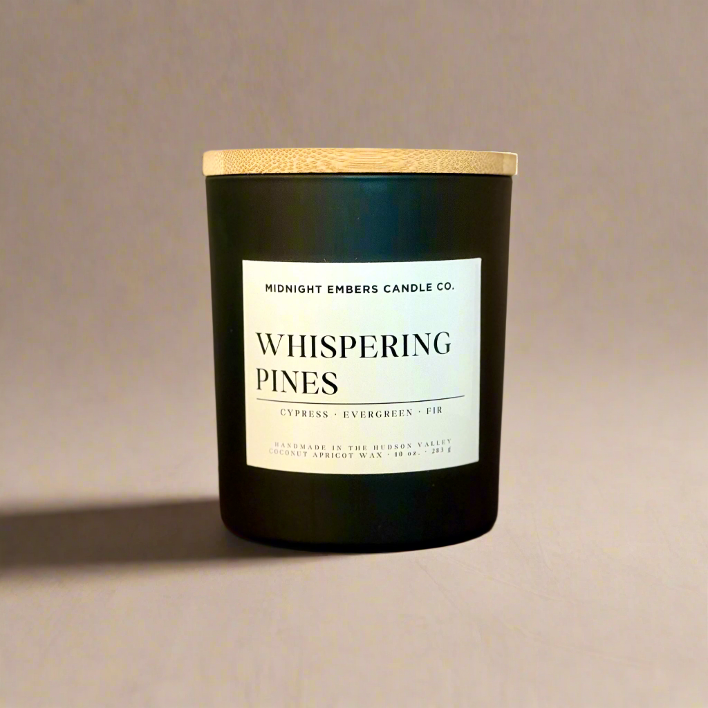 Black candle with a wooden lid and 'Whispering Pines' label on a beige background