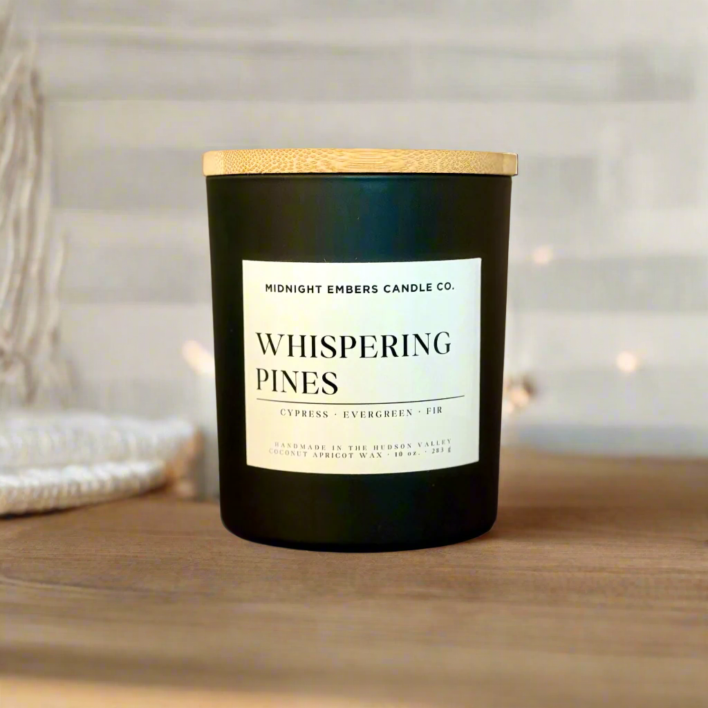 Black candle with a wooden lid and 'Whispering Pines' label on a beige background