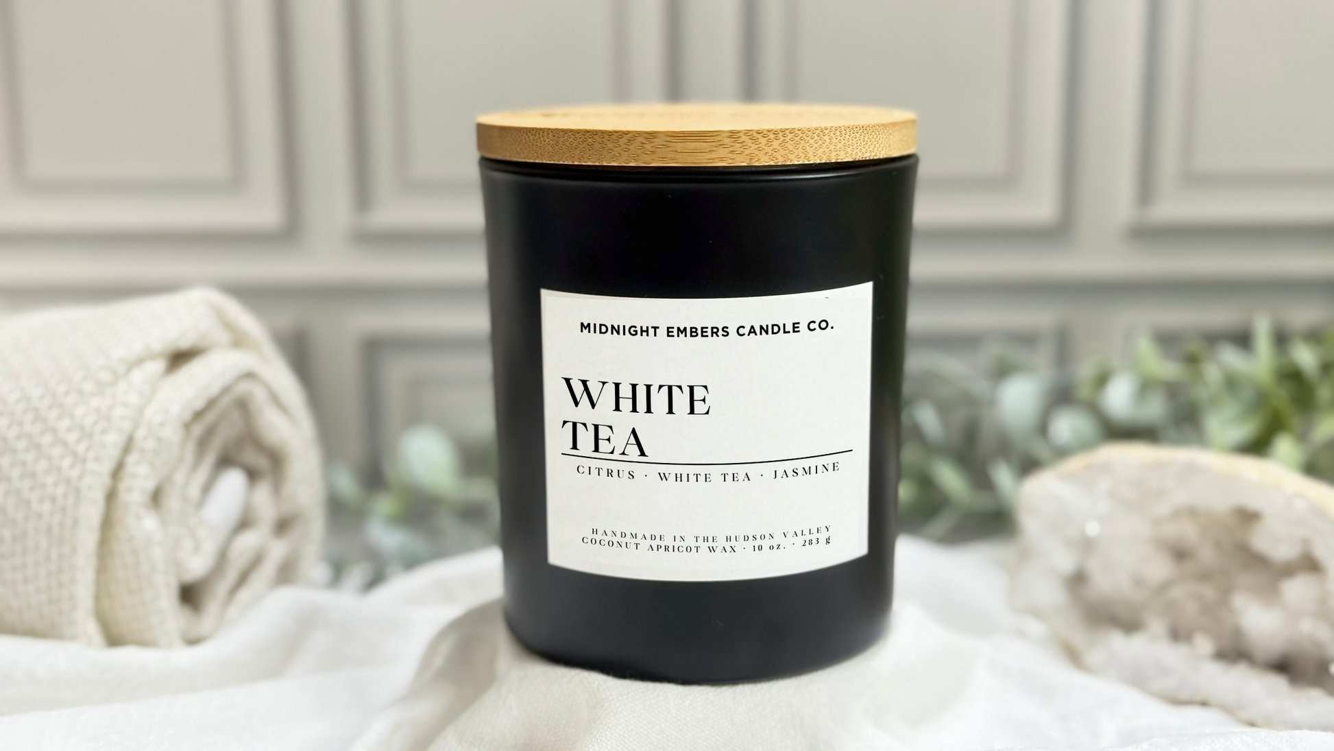 Black candle labeled 'White Tea' with a wooden lid on a white surface.