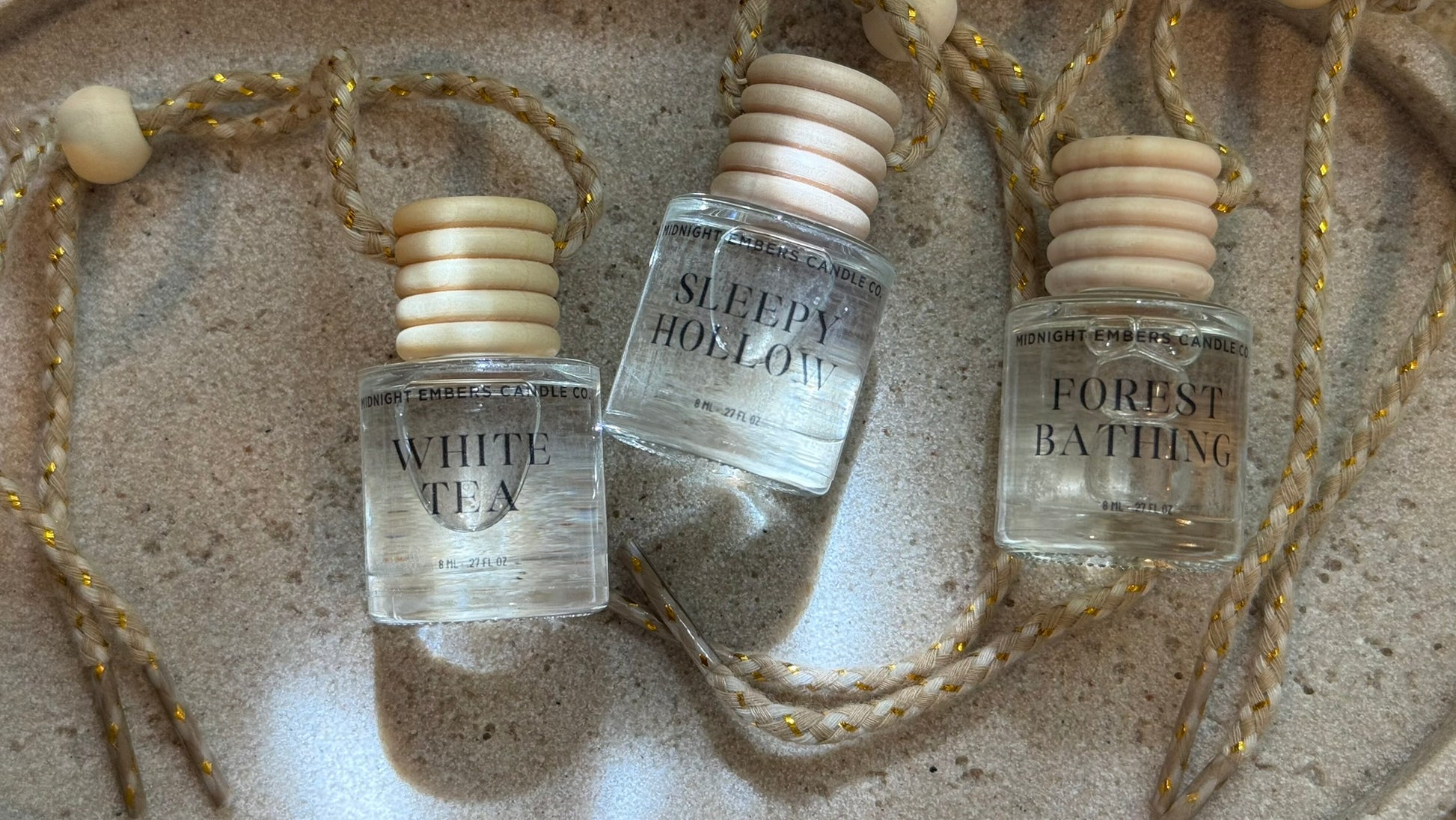 Three small bottles labeled 'White Tea', 'Sleepy Hollow', and 'Forest Bathing' on a textured surface.