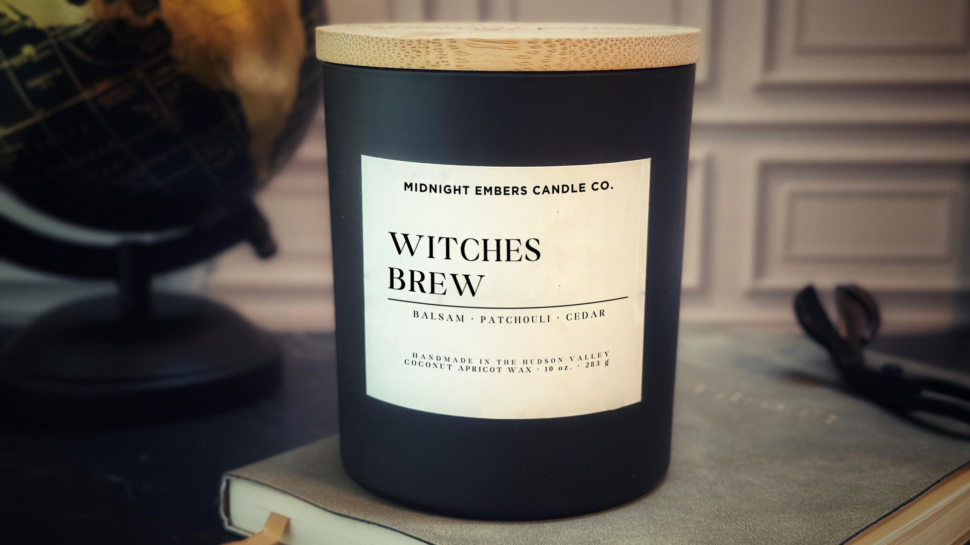 Black candle labeled 'Witches Brew' from Midnight Embers Candle Co. on a surface with a blurred background.